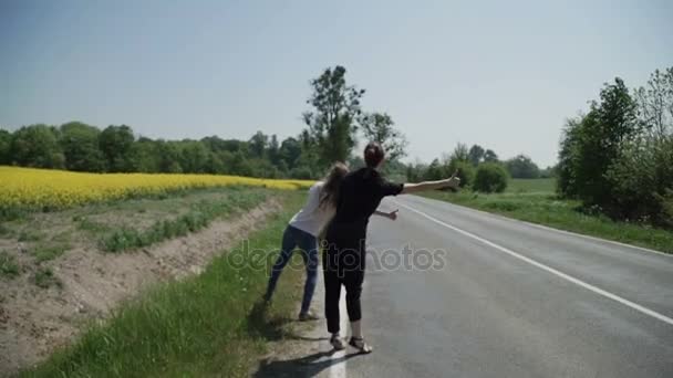 Két fiatal nők stopposok állni a pálya szélén, és kérni, hogy hagyja abba az elhaladó autók — Stock videók