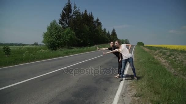Twee jonge vrouwen lifters staan aan de zijlijn en vragen om te stoppen met de passerende auto 's — Stockvideo
