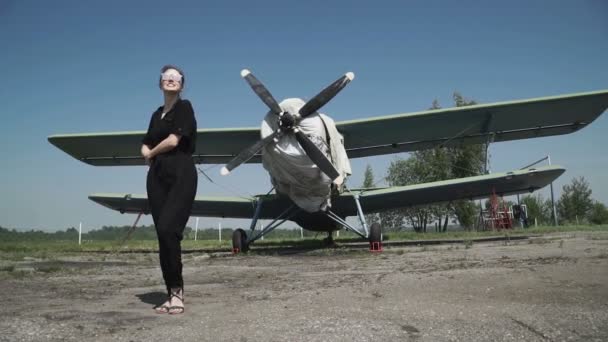 Donna pilota ritratto di fronte bombardiere aereo. in una combinazione nera in piedi di fronte a un'enorme elica d'aria — Video Stock