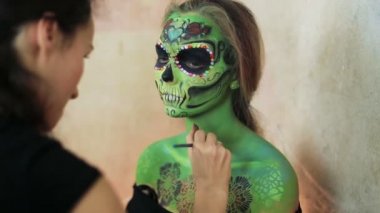 aquagrim yüz sanat halloween makyaj elleri üzerinde yapıyor kadın sanatçı yeşil korkunç göz kamaştırıcı rhinestones iskelet püsküller. Meksikalı Prenses şeker kafatası.