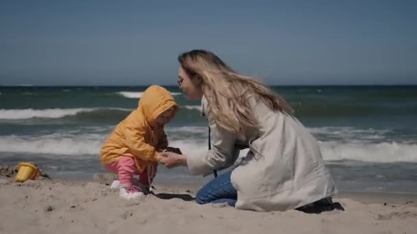 Genç anne ve küçük kız baharda deniz kıyısında sarı ceketlerle. — Stok video