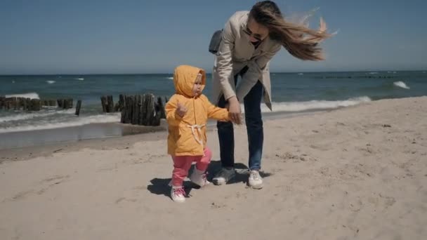 Jonge moeder en dochtertje aan de zeekust in het voorjaar in gele jassen — Stockvideo