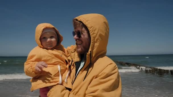 Apa és lánya azonos sárga kabátban boldogok, emeljék fel a kezüket a tengeren. — Stock videók