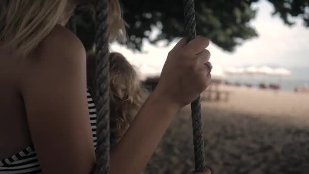 Jong moeder op een swing met een klein krullend meisje op een zee pak in de zomer — Stockvideo