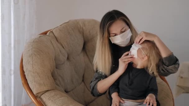 Jung mutter im ein medical mask puts ein mask auf sie tochter, aber die mädchen takes ab — Stockvideo
