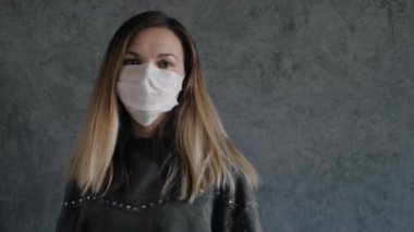 Genç bir kadın gri duvara karşı koruyucu bir maske takıyor.