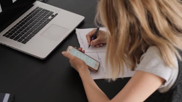 Młoda kobieta siedząca przy biurku, ucząca się online, laptop i smartfon — Wideo stockowe