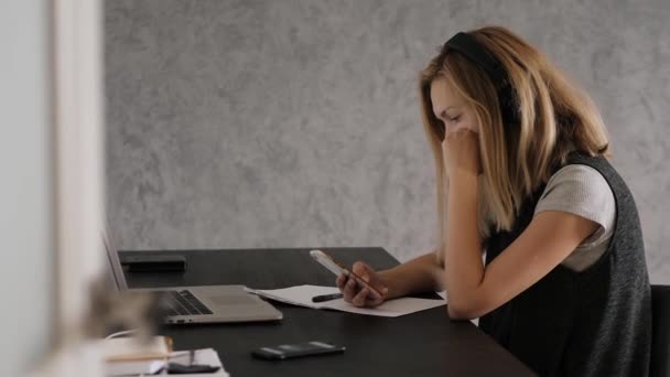Молодая женщина сидит за столом, онлайн обучение, ноутбук и смартфон — стоковое видео