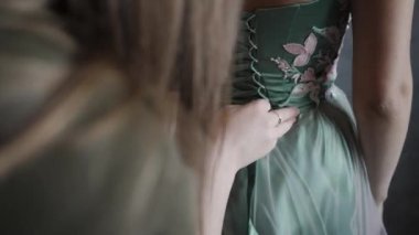 Korse bağcıklarını bağlayan kadın pembe çiçeklerle yeşil elbiseler giyiyor.