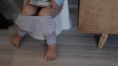Küçük kız elinde akıllı bir telefonla tuvalette oturuyordu.