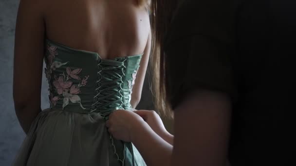 Woman tying the laces of the corset evening dresses green with pink flowers — Stock Video