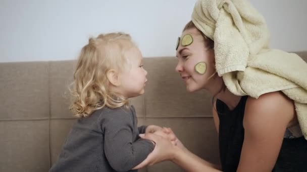 年轻的母亲和小女儿戴着白色的面具，脸上挂着黄瓜，亲吻着 — 图库视频影像