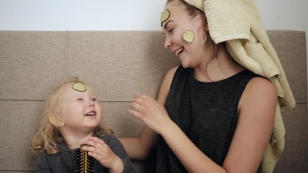 Jeune mère et petite fille, masque blanc appliqué avec des concombres sur le visage — Video