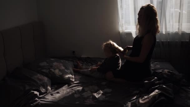 一位年轻的母亲在家里做一个坐在床上的发式小女孩 — 图库视频影像