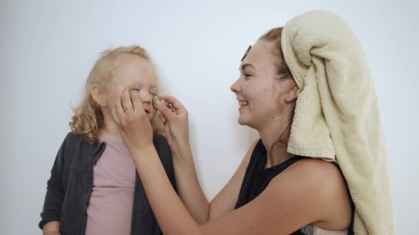 Νεαρή μητέρα και μικρή κόρη, εφαρμοσμένη λευκή μάσκα με αγγούρια στο πρόσωπο — Αρχείο Βίντεο