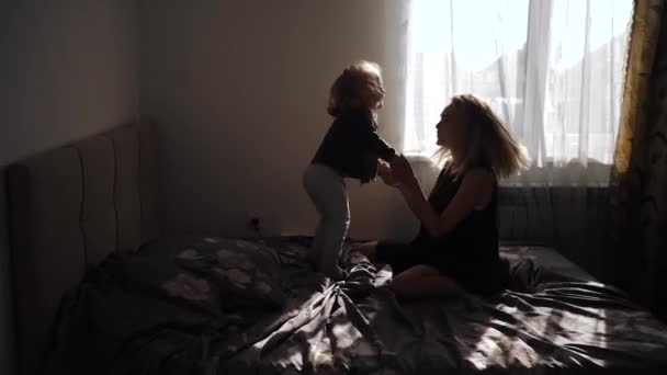 Gelukkig moeder en dochtertje samen springen op het bed thuis — Stockvideo