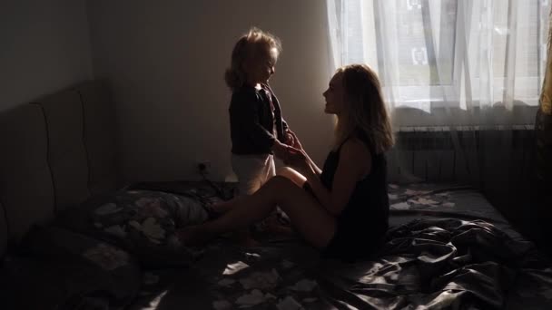 Feliz madre e hija pequeña juntos saltando en la cama en casa — Vídeos de Stock