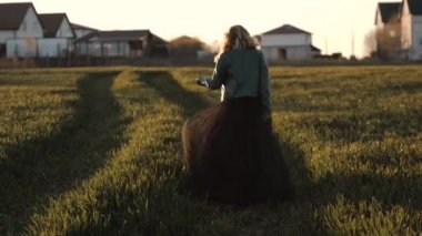 Uzun siyah elbiseli ve deri ceketli genç bir kadın tarlada koşuşturuyor.