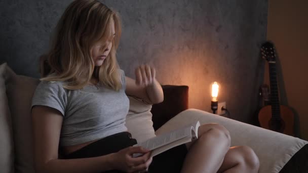 집에서 소파에 앉아서 책을 읽고 있는 젊은 여자 — 비디오