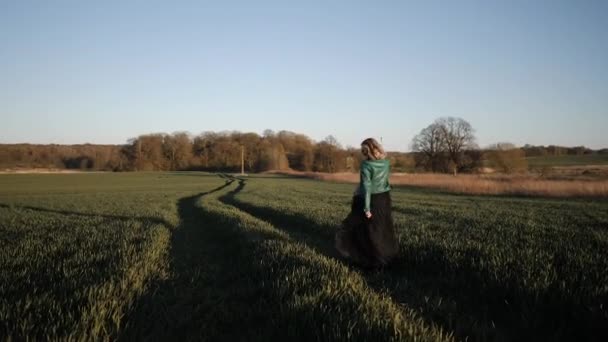 Mujer joven en un vestido largo negro y chaqueta de cuero corriendo por el campo — Vídeos de Stock