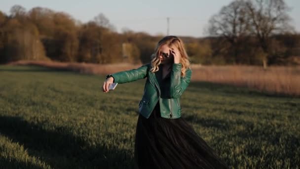 Jovem mulher em um longo vestido preto e jaqueta de couro correndo em torno do campo — Vídeo de Stock