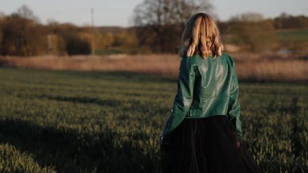 Mujer joven en un vestido largo negro y chaqueta de cuero corriendo por el campo — Vídeos de Stock