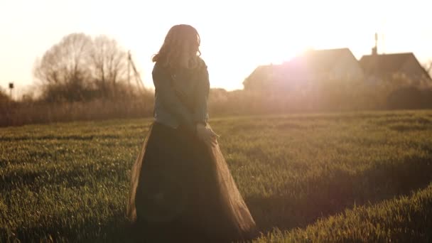 Mujer joven en un vestido largo negro y chaqueta de cuero corriendo por el campo — Vídeo de stock