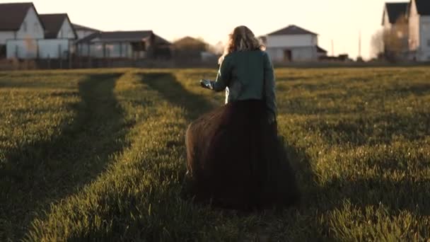 Mujer joven en un vestido largo negro y chaqueta de cuero corriendo por el campo — Vídeo de stock