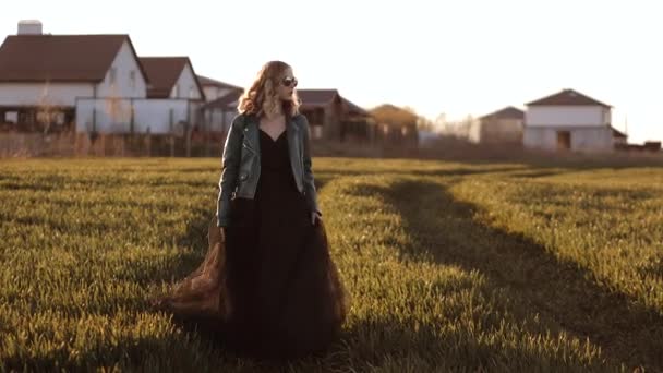 Junge Frau in langem schwarzen Kleid und Lederjacke läuft auf dem Feld herum — Stockvideo