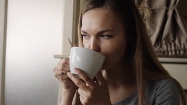 Bir kafede kahve içen genç bir kadın.