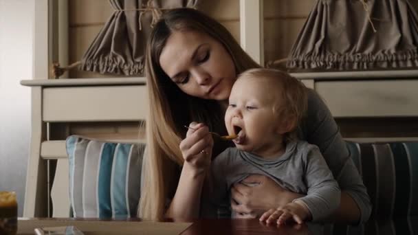 Мать кормит маленькую девочку пюре ложкой — стоковое видео