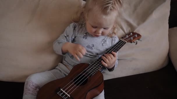Liten flicka spelar ukulele och går till sängs titta på kameran — Stockvideo