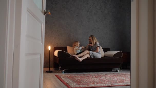 Eine junge Frau mit einer kleinen Tochter spricht auf der Couch im Wohnzimmer — Stockvideo