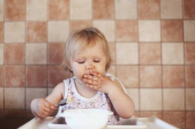 Küçük kız öğle yemeğini beyaz çocukların masasında yiyor.