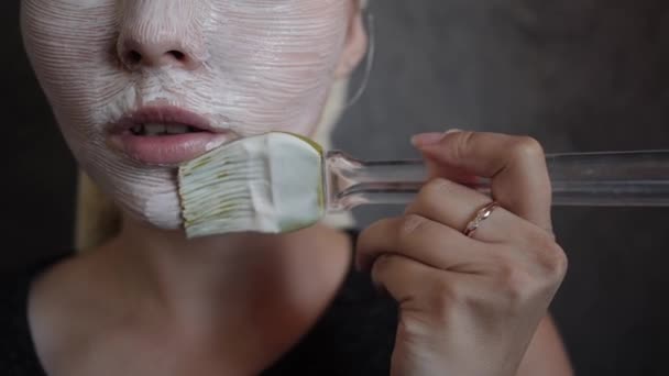 Eine junge Frau mit einer weißen Maske aus Creme im Gesicht mit Pinsel Nahaufnahme — Stockvideo