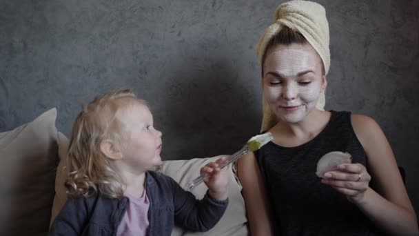 Молодая мать и маленькая дочь в белой маске с огурцами на лице — стоковое видео