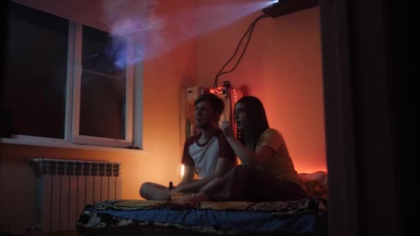 Jeune couple homme et femme regardant un film home cinéma projecteur en fumée — Video