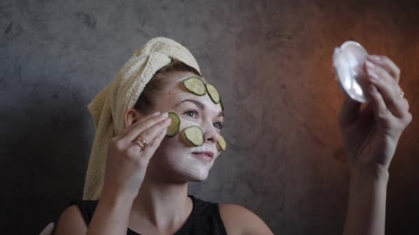 Uma jovem recebe uma máscara facial branca com pepinos home care — Vídeo de Stock