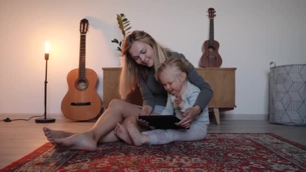 Fiatal anya és lánya ül a padlón, és beszél videokapcsolattal — Stock videók