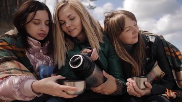 Три молодые женщины на природе пьют горячий чай, завернутый в одеяло — стоковое видео