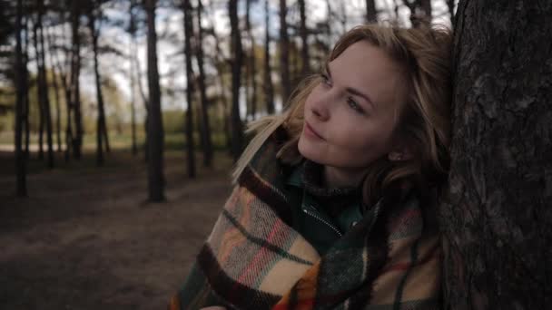 Молода жінка в лісі біля дерева насолоджується свіжим повітрям у теплій ковдрі — стокове відео