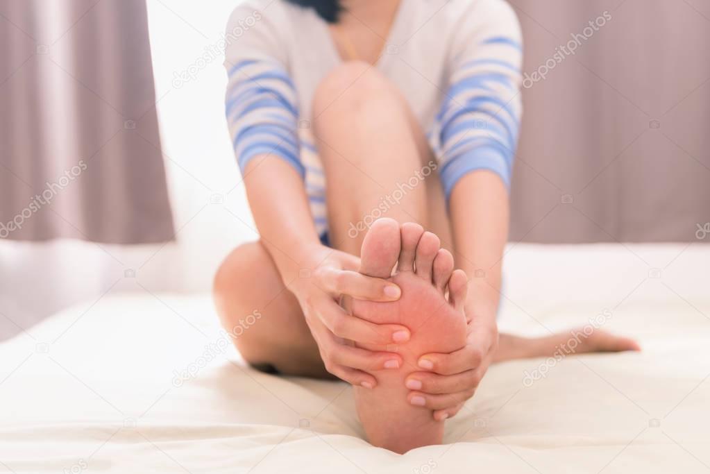 Young woman massaging her foot on the bed, Healthcare concept
