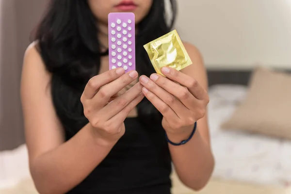 Mulher asiática segurando preservativo e pílulas anticoncepcionais — Fotografia de Stock