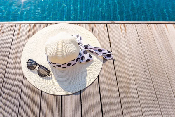 Straw sun hat and sunglasses on the terrace of swimming pool