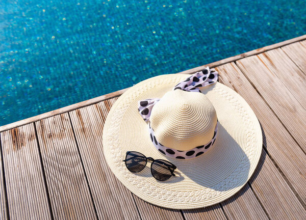 Соломенная шляпа и солнцезащитные очки на террасе бассейна

