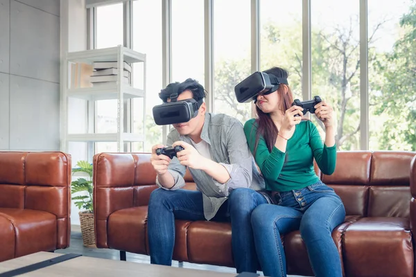 Young Couple Having Fun While Playing Virtual Reality Game Together in Their Home. Couple Love Having Enjoyment With Electronic VR Goggles Gaming on Couch. Entertainment Innovation/Lifestyles Concept