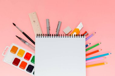 Pembe arka planda sarmal not defteri altında renkli okul malzemeleri ve mesaj için yer var. Farklı renklerin kırtasiyesi.