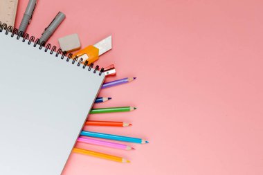 Pembe arka planda sarmal not defteri altında renkli okul malzemeleri ve mesaj için yer var. Farklı renkte kırtasiye malzemesi. Okul konseptine dönelim..