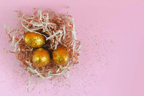 Huevos dorados de Pascua en nido sobre fondo rosa. Mínimo espacio de copia de concepto de Pascua para texto. Vista superior, plano . — Foto de Stock