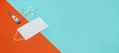 Beyaz tıbbi koruyucu maske, haplar ve mavi arka planda termometre. Coronovirus önleme ve sağlık hizmeti kavramı. Üst yatay görünüm telif uzayı